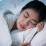 Gambar secangkir teh chamomile di meja samping tempat tidur, menggambarkan penggunaan remedi alami untuk mendukung tidur yang lebih baik.