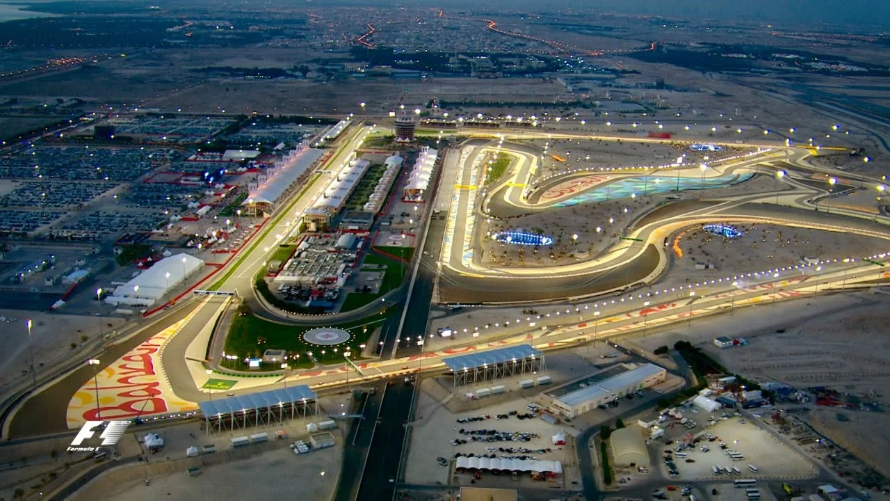 Formula 1 cars racing wheel-to-wheel under the floodlights at the Bahrain Grand Prix, highlighting the intense competition.