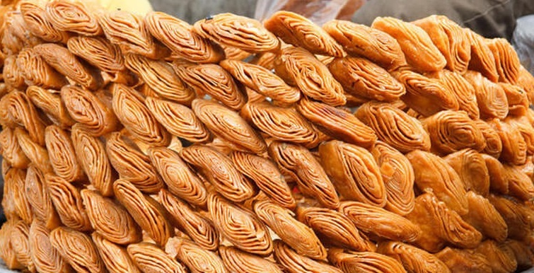 A plate of golden-brown Khaja, stacked in layers, with a drizzle of sugary syrup, representing the traditional Indian delicacy's visual appeal and sweetness.