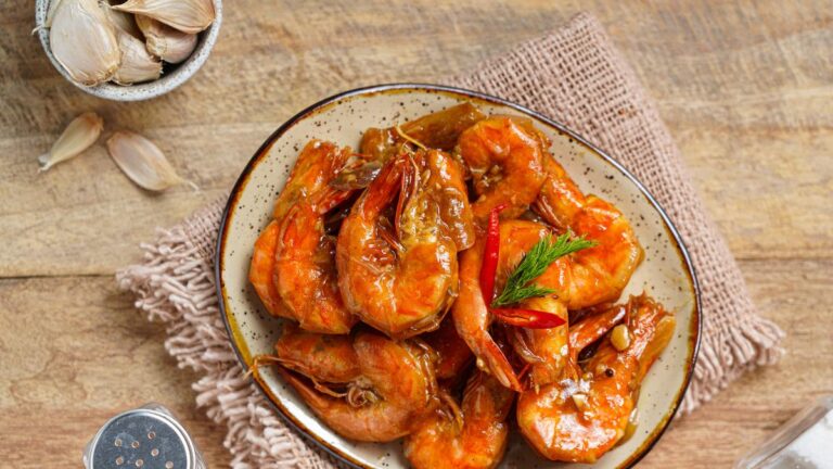 Hidangan udang asam manis yang menggugah selera, disajikan dengan saus kental berwarna merah cerah dan taburan daun bawang segar