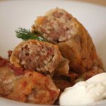 Close-up of freshly prepared Sarmale stuffed cabbage rolls served with a dollop of sour cream and fresh dill on top.