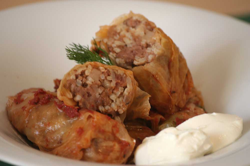 Close-up of freshly prepared Sarmale stuffed cabbage rolls served with a dollop of sour cream and fresh dill on top.