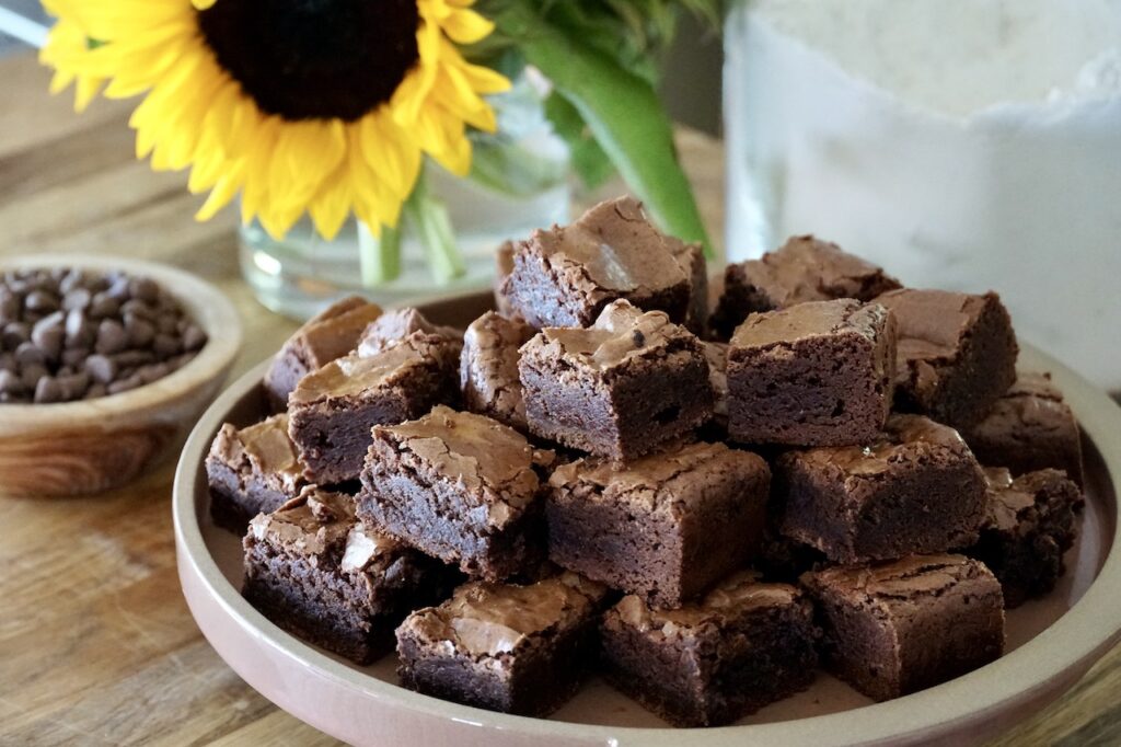 Fudgy Brownies Lezat: Potongan fudgy brownies yang tebal dan lembut, dengan permukaan yang retak sempurna, siap disantap